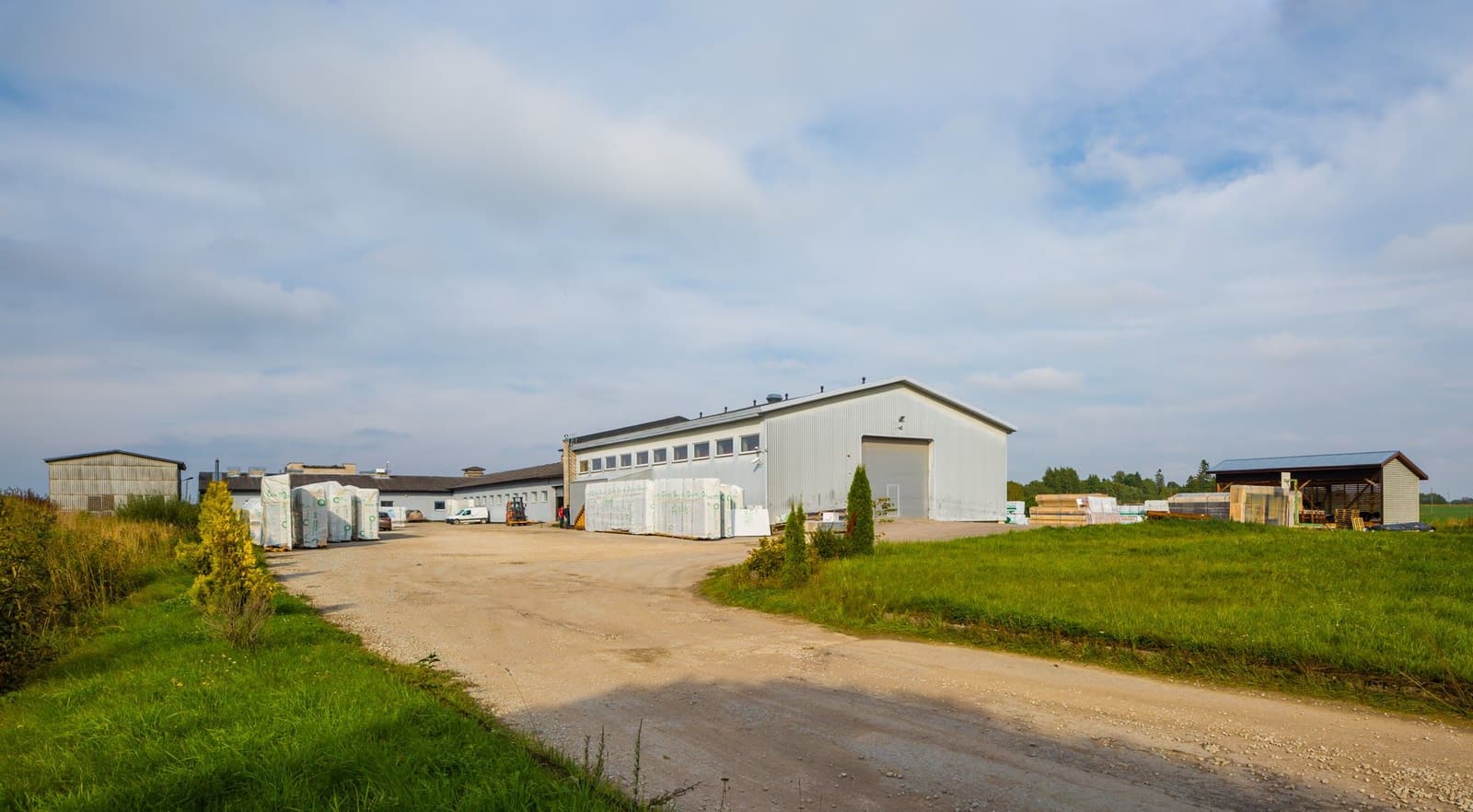 The factory yard with weather-wrapped wall-element packages staged outside the production halls, ready for transport