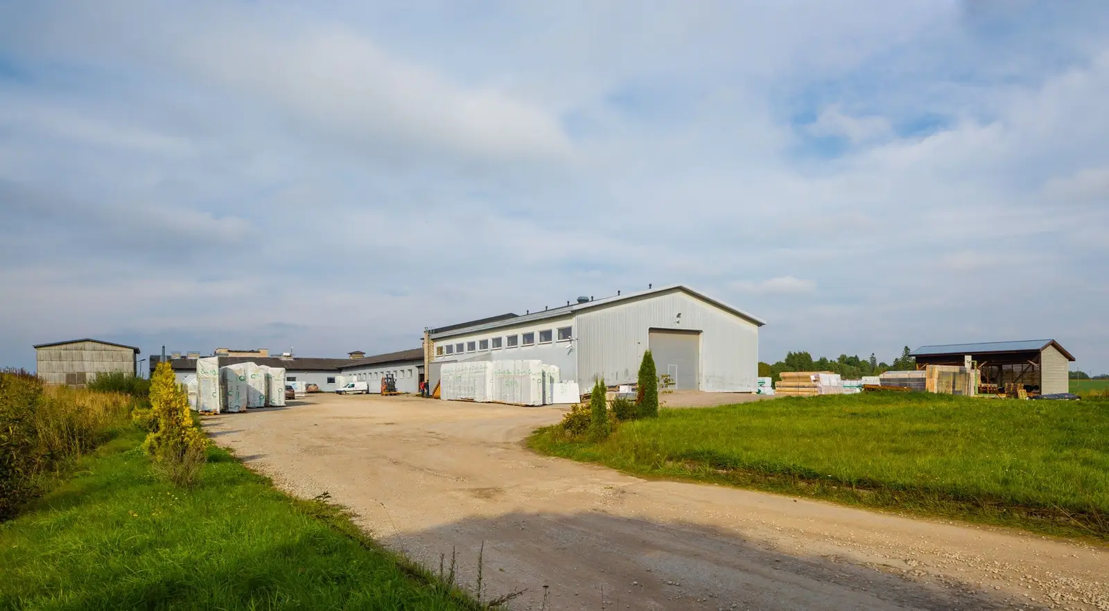 The factory yard with weather-wrapped wall-element packages staged outside the production halls, ready for transport